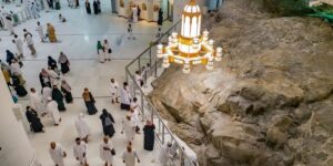Pilgrims in white ihram walking past the rocky hill of Safa under a large gold chandelier in the Grand Mosque