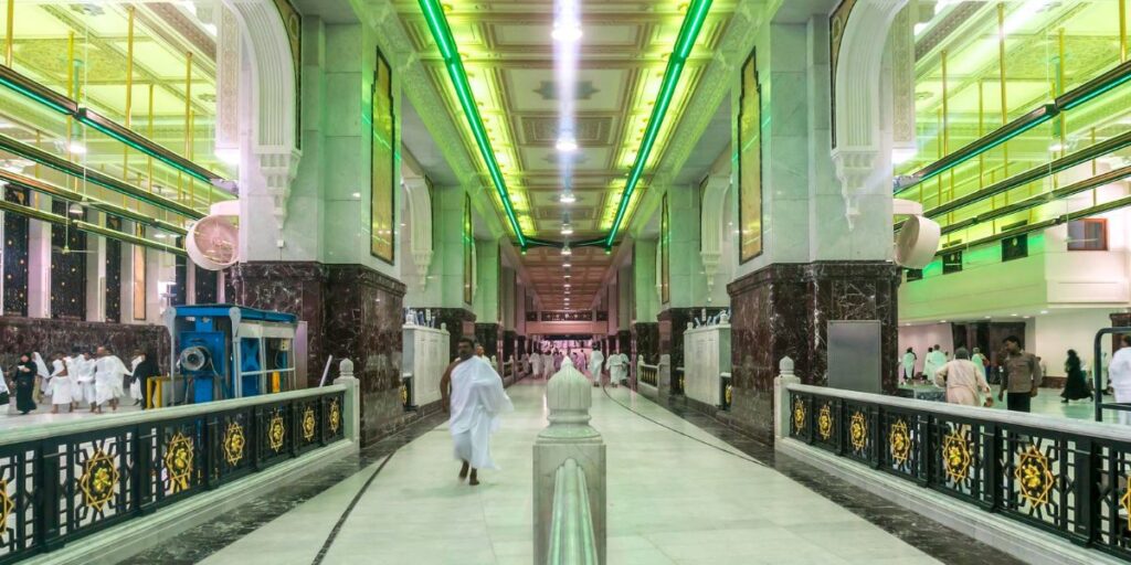 A man in white ihram runs through the Mas'aa gallery under green lights during the Sa'i ritual in Mecca