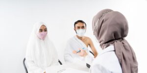 Two pilgrims wearing face masks consult with a healthcare professional in a bright, clinical medical setting